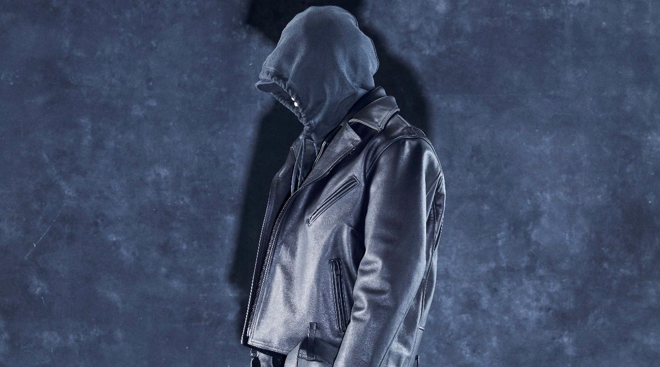 Person wearing a dark leather jacket with hood against a textured blue background